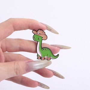 Close-up of a cute green dinosaur enamel pin with a pink cowboy hat and pink boots
