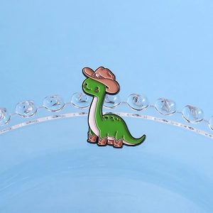 Spilla creativa con dinosauro verde che indossa cappello da cowboy e stivali su vetro