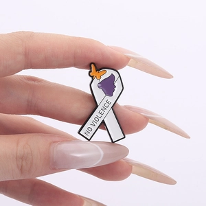 Macro shot of white enamel ribbon pin with purple silhouette and NO VIOLENCE slogan