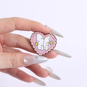 Detail view of heart-shaped cat paw enamel pin with pink border held by a hand