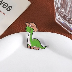 Détail d'un pin's dinosaure vert portant un chapeau de cow-boy sur un plat blanc