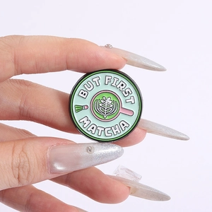 Close-up of circular enamel pin featuring 'But First Matcha' slogan and latte art