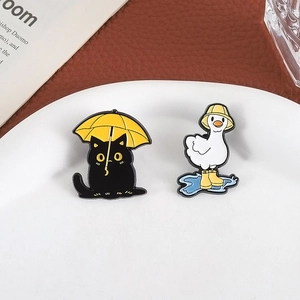 Detailed view of cute enamel cat and duck pins with vibrant yellow umbrella on a plate