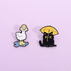 Detail of enamel pins featuring a white duck in rain boots and a black cat with an umbrella