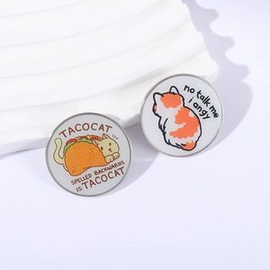 Funny enamel pins featuring Tacocat palindrome and angry cat meme on white pedestals