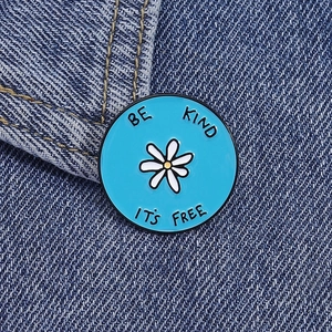 Detail of blue enamel daisy brooch with Be Kind It's Free text on denim fabric