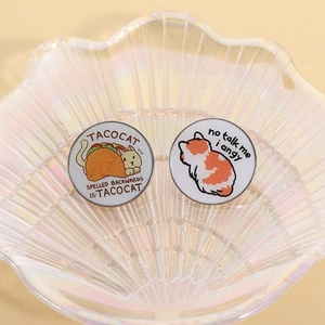 Detailed close-up of cute enamel pins featuring Taco Cat and Angy Cat on a shell tray