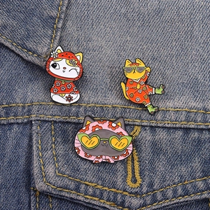 Tre spille smaltate a forma di gatti cartone con abiti floreali su sfondo denim blu