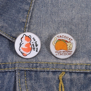Detailed view of two cartoon cat enamel pins on a dark blue denim jacket collar