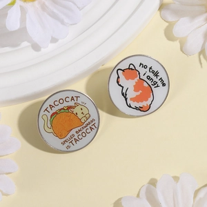 Cute cartoon taco cat and calico enamel pins displayed on a minimalist white stand