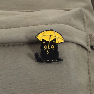 Cute black cat with yellow umbrella enamel pin on a khaki fabric bag accessory
