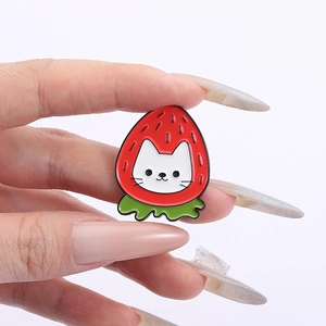 Close-up of strawberry cat enamel pin held by fingers showing fine metal textures
