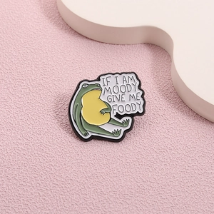 Detailed view of frog enamel pin featuring If I Am Moody Give Me Foody text on pink base