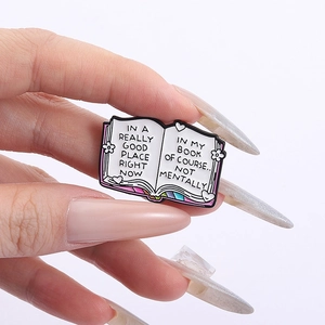 Detail shot of hand-held open book enamel pin with humorous English quotes and pink spine