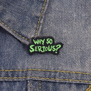 Gros plan d'une broche en émail noir avec texte Why So Serious sur revers en jean bleu