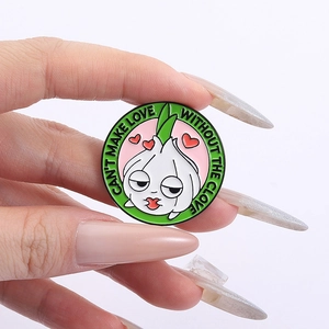 Detail of cartoon garlic enamel pin with humorous text held in hand against white