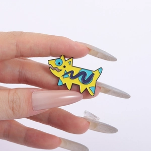 Détail d'une broche chiot en émail jaune avec pois bleus et vagues mauves tenue à la main