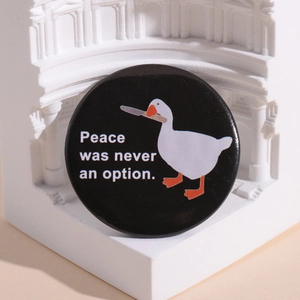 Badge rond en fer-blanc avec une oie de dessin animé tenant un couteau sur fond noir