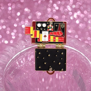 Detail view of an opening suitcase enamel pin with magic school scarf and glasses
