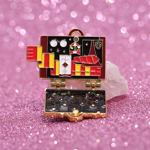 Enamel suitcase brooch featuring magic school icons on a pink glitter background