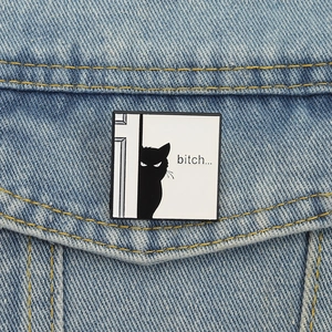 Detailed view of quirky black cat enamel pin on a denim jacket pocket featuring text