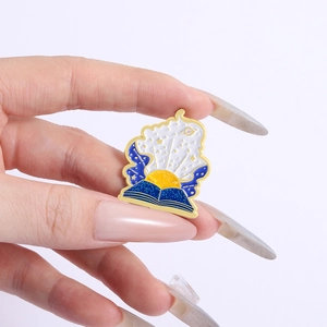 Detail showing hand holding an enamel starry sky book brooch with stars and sun