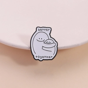 Detail showing white enamel pin with two cartoon figures hugging and Better Together text