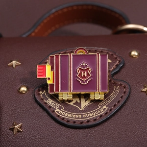 Macro detail of brown leather bag with Hogwarts crest pin and gold star studs
