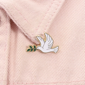 Détail du pin's colombe blanche en émail avec branche d'olivier sur col en jean rose