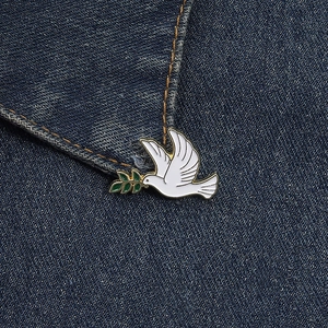 Gros plan détaillé d'une broche colombe en émail blanc avec rameau d'olivier sur jean