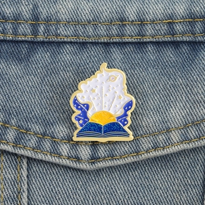 Starry night magic book enamel pin with moon and stars on blue denim jacket