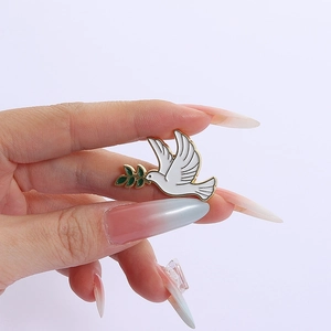 Détail macro d'une broche colombe de paix en émail blanc avec des ailes dorées et olivier