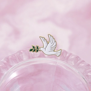 Macro d'une broche colombe en émail blanc aux bords dorés sur le bord d'un verre rose