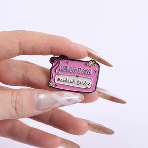 Pink enamel pin featuring Bookish Girlie text and cute bow decorations held in hand