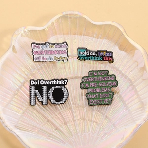 Detailed view of four funny overthinking enamel pins on an iridescent shell tray