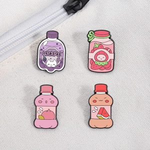 Close-up of four cute cartoon fruit juice bottle enamel pins on a white canvas bag texture