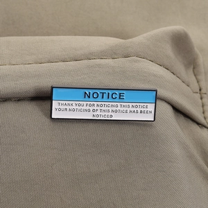 Macro shot of rectangular blue and white enamel pin with humorous NOTICE text quote