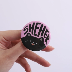 Close-up of pink round badge featuring a black cat icon and SHEHER text lettering