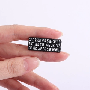 Detail of funny rectangular cat brooch with quotes held in hand on white background