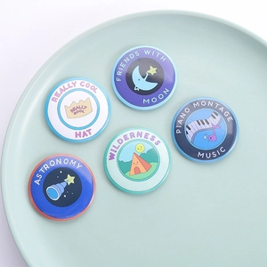 Detailed close-up of five cute cartoon tinplate badges with moon and piano designs