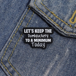 Détail macro d'un pin's émaillé à slogan humoristique noir et blanc sur veste en jean