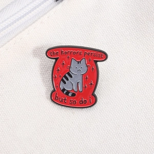 Détail macro de broche en émail montrant un chat gris sur fond rouge et texte