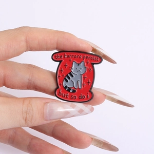 Pin's en émail avec chat gris sur fond rouge et texte the horrors persist but so do i