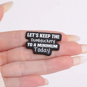 Vue rapprochée d'un badge en PVC noir tenu à la main avec une citation humoristique gravée