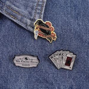 Détail des épingles émaillées The Crow Club avec corbeau, rose et cartes sur denim