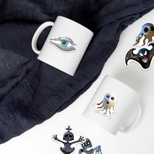 Close-up of surreal gothic skull stickers applied to a white glossy ceramic mug surface