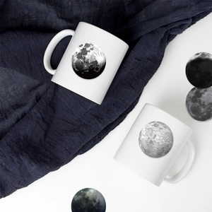 Set of two white ceramic moon mugs with realistic lunar prints on blue fabric background
