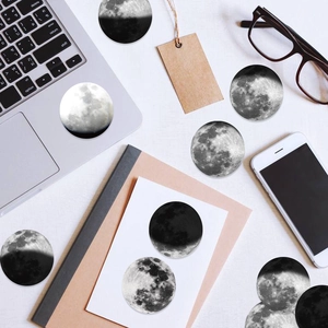 Flat lay of circular moon phase stickers on a desk with laptop and lifestyle props