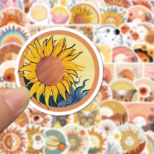 Close-up of bohemian sun and flower stickers held by hand for laptop and guitar deco