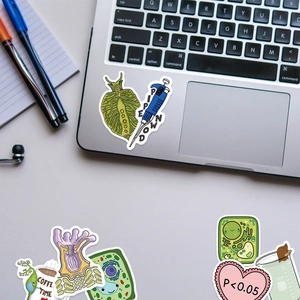 Close-up of waterproof biology lab stickers on a laptop featuring scientific puns and cells